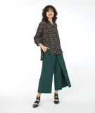 model in a black terrazzo print button down blouse with a mandarin style collar and a low drape in the back, worn with a wide leg green pant