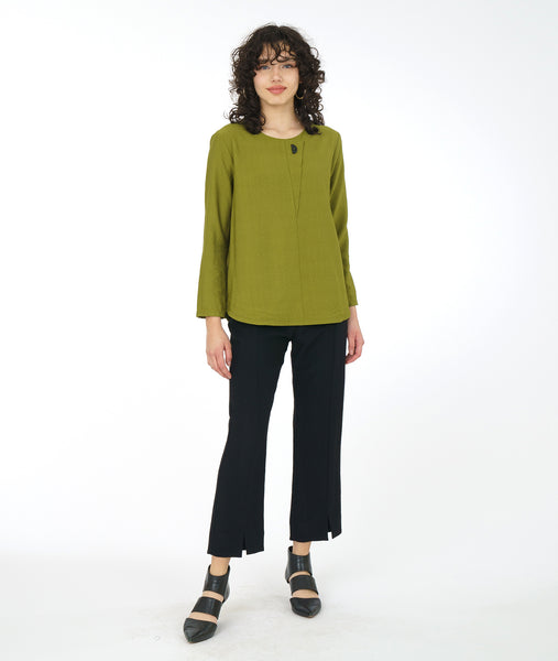 model in a green long sleeve top with a triangular panel and button at the neckline, worn with a slim black pant