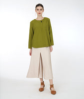 model in a green long sleeve top with a triangular panel and button at the neckline, worn with a wide leg ivory pant