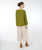 model in a green long sleeve top with a triangular panel and button at the neckline, worn with a wide leg ivory pant