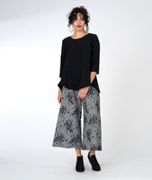 model in a wide leg grey and black print pant with a black pull over top with 3/4 sleeves and a high-low hem