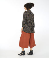 model in a black terrazzo print button down blouse with a mandarin style collar and a low drape in the back, worn with a wide leg rust color pant