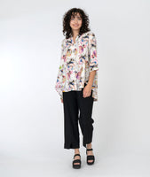 model in a slim black pant with a floral print button down blouse with a full flowing back