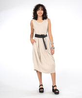 model in a sleeveless oatmeal color dress with tucks at the waist and a black belt