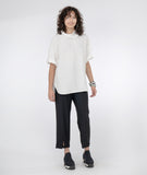 Model in a slim black pant with a white pull over top with a cowl neck