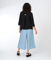 model in a black button down blouse with a flowy body and a wide leg blue pant